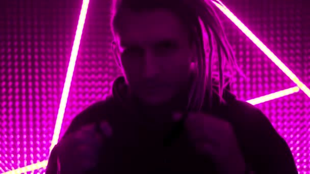 Young guy model in neon lights. Neon triangle in a club studio. Concept of dubstep or punk style. Wearing a medical black mask. Protected in a public place from the Chinese coronavirus — Stock Video