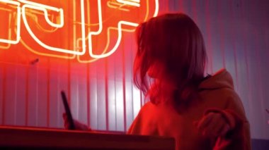 Güneş gözlüklü şık kız blogcu akıllı telefon kullanarak selfie ya da video çekiyor. Çekici esmer genç kadın kendine cep telefonuyla bakıyor ve kısa saçlarına dokunuyor. Kırmızı neon ışık.