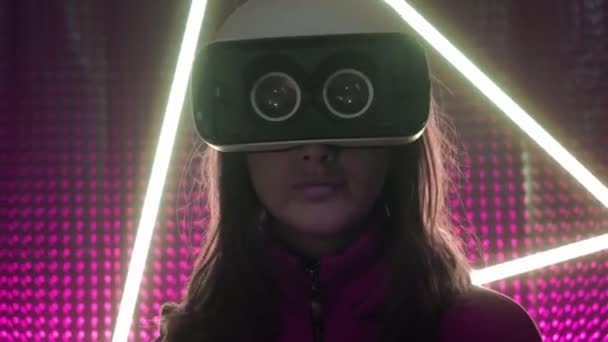 Νεαρή κοπέλα επαγγελματίας gamer φορώντας γυαλιά εικονικής πραγματικότητας. Βυθισμένο σε μια παράλληλη πραγματικότητα, δημιουργεί αρχιτεκτονικά αντικείμενα. Φουτουριστικό λευκό VR γυαλιά. Ο σχεδιαστής δημιουργεί νέα τέχνη. — Αρχείο Βίντεο