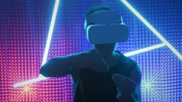 Νεαρός επαγγελματίας παίκτης με γυαλιά εικονικής πραγματικότητας. Βυθισμένο σε μια παράλληλη πραγματικότητα, δημιουργεί αρχιτεκτονικά αντικείμενα. Φουτουριστικό λευκό VR γυαλιά. Ο σχεδιαστής δημιουργεί νέα τέχνη. — Αρχείο Βίντεο