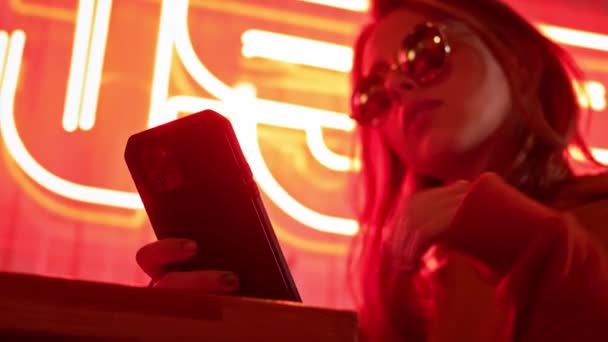 Portrait d'une jolie fille souriante utilisant les médias sociaux en ligne et écoutant de la musique. Jolie jeune femme tapant message sur smartphone et sourire. Style de rue décontracté habillé. Fluo rouge coloré . — Video