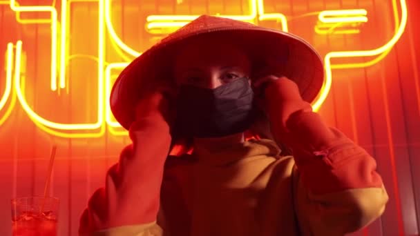 Концепция пандемии коронавируса. Женщина в городской защитной или медицинской маске, смотрящая на камеру на неоновом фоне. Защита и профилактика болезни 2019-nCoV. 4k — стоковое видео