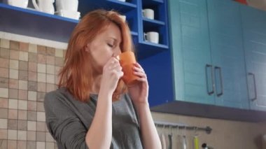 Kızıl saçlı çekici kız sabah kahvesini ev mutfağında içiyor. Freelancer sabahı. Mutfakta uykulu bir sabahın tadını çıkarıyor..