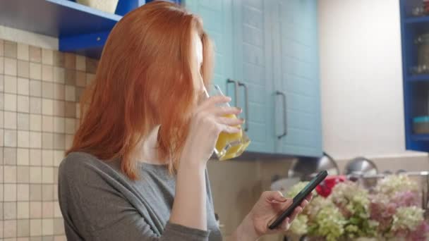 Mooi meisje die vers sinaasappelsap drinkt uit glas. Gelukkige vrouw die fruitdrank drinkt. Mooi meisje in t-shirt in de keuken. Gezonde en natuurlijke voeding. Gezond ontbijt in het weekend — Stockvideo