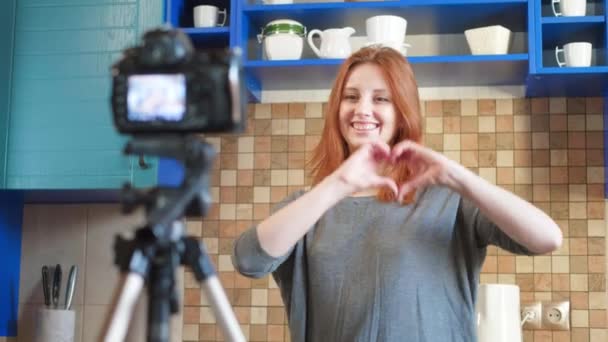 Food-Bloggerin und Influencerin nimmt in der Küche ein Video oder einen Podcast auf. Macht Lifestyle-Blog vlog, zeigt ein Herzzeichen von den Händen. Eine Frau kommuniziert mit Abonnenten, bittet, das Video zu mögen. — Stockvideo