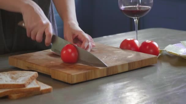 Vrouw snijdt club sandwich in tweeën met scherp mes op een houten plank in de keuken, het maken van de fastfood thuis. Een close-up. Meisjes handen gesneden tomaten voor een sandwich, ontbijt. — Stockvideo