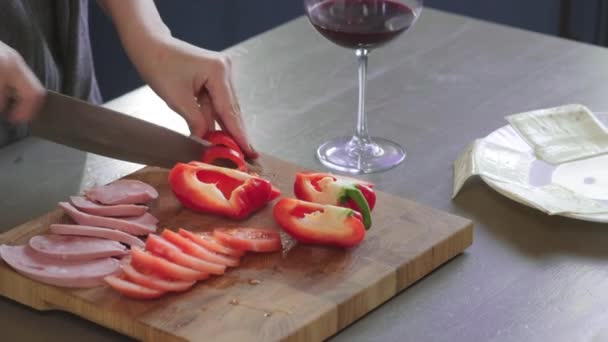 Kvinna skär klubbsmörgås i en halv av vass kniv på en träskiva i köket, gör av snabbmat hemma. Närbild. Flickor händer hacka bell pepper för en smörgås, frukost. — Stockvideo