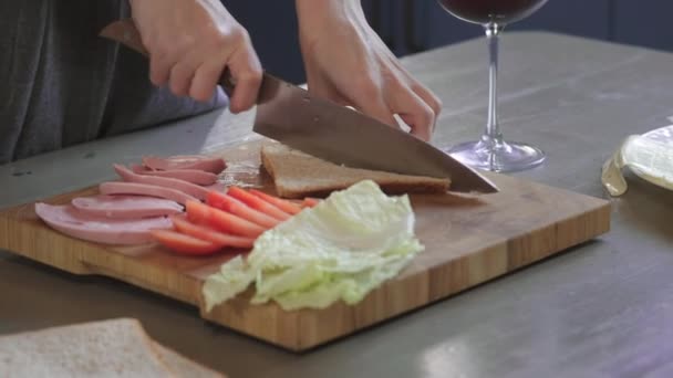 Mujer corta sándwich de club en una mitad por cuchillo en una tabla de madera en la cocina, haciendo de la comida rápida en casa, chef está cocinando sándwich. Primer plano. Las niñas cortan el pan para un sándwich, el desayuno — Vídeo de stock