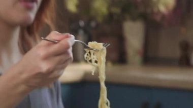 Çekici kızıl saçlı kız mutfakta çatalla hazır erişte yiyor. Plastik bir kutudan abur cubur yiyor. Kötü bir yaşam tarzı. Yemek hareket halinde. Asya Tavası Yiyen Kadın Paket Paketinden Erişte.