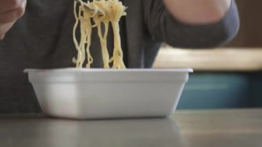 Çekici kızıl saçlı kız mutfakta makarna, makarna ve peynir yiyor. Abur cubur yiyor. Kötü bir yaşam tarzı. Telefonla konuşuyorum. Yemek hareket halinde. Özel plastik tabakta demlenmiş sarı ramen.