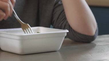 Çekici kızıl saçlı kız mutfakta makarna, makarna ve peynir yiyor. Abur cubur yiyor. Kötü bir yaşam tarzı. Telefonla konuşuyorum. Yemek hareket halinde. Özel plastik tabakta demlenmiş sarı ramen.