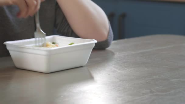 Chica pelirroja atractiva come fideos instantáneos con un tenedor en la cocina. Come comida chatarra de una caja de plástico. Mal estilo de vida. Comida en movimiento. Mujer comiendo fideos wok asiáticos de Take away Box . — Vídeo de stock