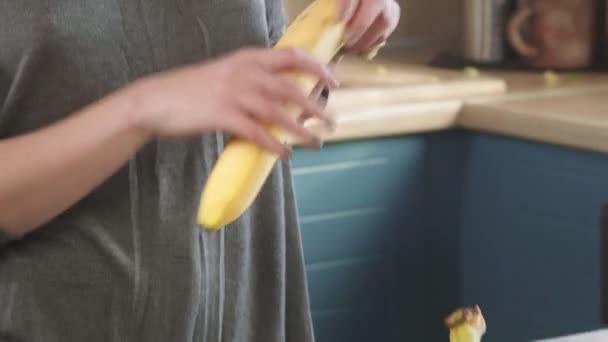 Ελκυστική πεινασμένη κοκκινομάλλα τρώει μια μεγάλη μπανάνα νωρίς το πρωί το Σαββατοκύριακο στην κουζίνα. Καθαρίζει τη φλούδα. Υγιεινή διατροφή, ο σωστός τρόπος ζωής. Πρωινό για σπορ. — Αρχείο Βίντεο