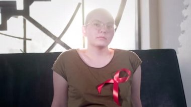 AIDS ya da HIV 'li kel bir kız evde oturuyor. Kırmızı kurdele takıyordu. Kemoterapiden sonra rehabilitasyon. Kanser farkındalığı kurdelesi.