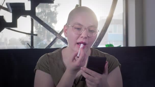 Лесбійська лисина хвора на рак. Жінка фарбує губи губною помадою, дивиться у дзеркало. Відновлення після хіміотерапії. Догляд за зовнішнім виглядом. Вірус заражений і допомагає. — стокове відео