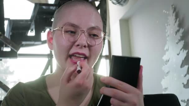 レズビアンのはげの女の子は癌で病気です。女は口紅で唇を塗り鏡を見る。化学療法後のリハビリ。外見を気にしてる。HIVは感染しエイズは. — ストック動画