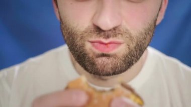 Yakın plan, sakallı bir adam hamburger yiyor. Tek eliyle çizburger tutuyormuş. Sağlıklı bir hayat sürmüyor, sağlık ve metabolizmayı bozuyor. Yanlış yemek.