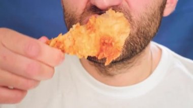 Yakın plan, fast food yiyen bir adam. Bir parça tavuk ısırıyor. Elinde nugget tutuyor. Sağlıklı beslenme ve kötü yaşam tarzıyla ilgili sorunlar. Kızarmış küçük tavuk. Abur cubur