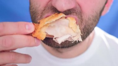 Yakın plan, fast food yiyen bir adam. Bir parça tavuk ısırıyor. Elinde nugget tutuyor. Sağlıklı beslenme ve kötü yaşam tarzıyla ilgili sorunlar. Kızarmış küçük tavuk. Abur cubur