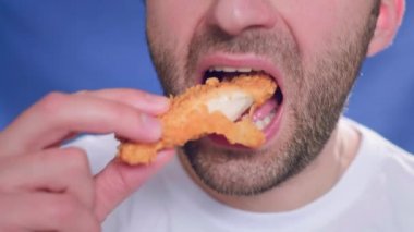 Yakın plan, fast food yiyen bir adam. Bir parça tavuk ısırıyor. Elinde nugget tutuyor. Sağlıklı beslenme ve kötü yaşam tarzıyla ilgili sorunlar. Kızarmış küçük tavuk. Abur cubur