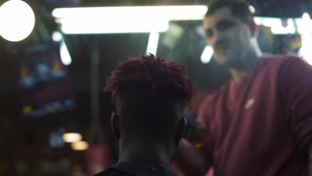 Afro-Amerikaan bij de kapper, maakt een baard. Aantrekkelijke Afro-Amerikaanse man krijgt een modern kapsel in de kapperszaak. Kapper plast haar door spray en kamt ze. Handschot. — Stockvideo