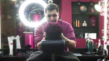 Yakın plan: bir kuaför bir Afrikalı Amerikalının saçlarını tıraş eder. Şık bir saç stili yapıyor, elektrikli tıraş makinesi kullanıyor. Dreadlock 'ların kafaları kırmızı..