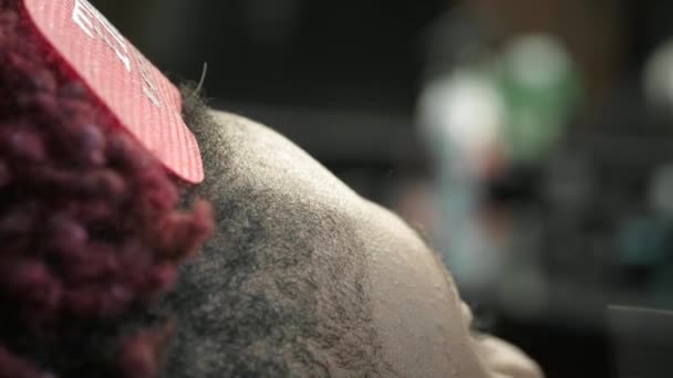 Крупный план: парикмахер сбривает волосы с головы афроамериканца. Делает стильные прически, использует электрический тример для бритья. Дредлоки красные на голове. . — стоковое видео