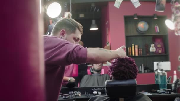 Nahaufnahme: Ein Friseur rasiert einem Afroamerikaner die Haare auf dem Kopf ab. Macht eine stylische Frisur, verwendet einen elektrischen Rasierapparat. Dreadlocks sind rot auf dem Kopf. — Stockvideo