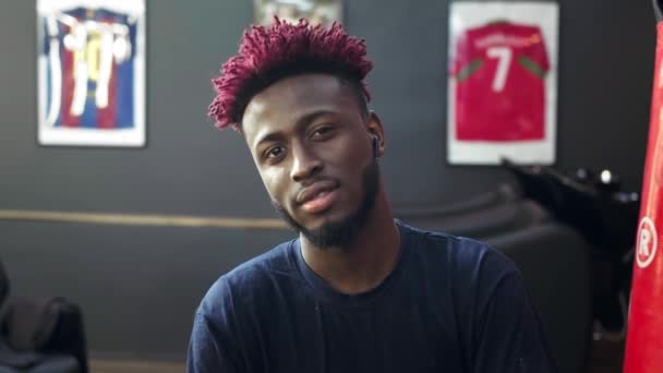 Portrait of a stylish young african american indoors. He looks at the camera, smiles seductively. Hair is colored red and braided in dreadlocks — Stock Video