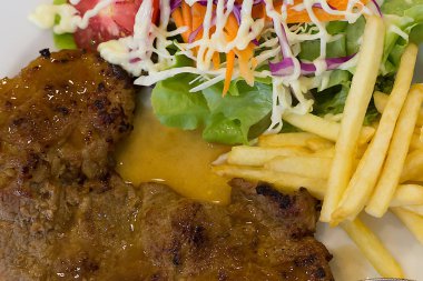 Patates kızartmalı biftek ve beyaz tabakta salata..