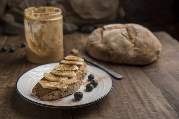 Vegan breakfast, slice of rustic bread, peanut butter and banana — Stock Photo, Image