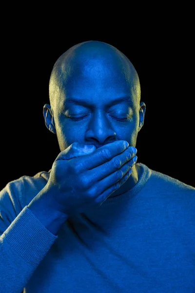 Eli eli ve gözleri kapalı siyah bir adam. Mavi jel filtresi ile ışık