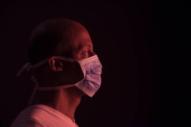 Coronavirus, koruyucu maskeli Afro-Amerikan bir adamın yan portresi. COVID-19 kavramı. Telif alanı ile koyu arkaplanda stüdyonun görüntüsü
