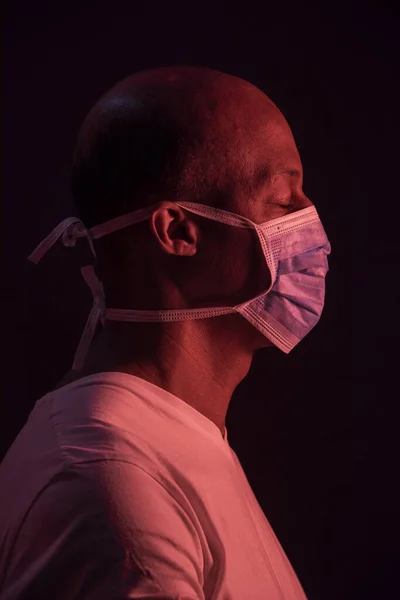 Coronavirus, koruyucu maskeli ve gözleri kapalı Afro-Amerikan bir adamın yan portresi. COVID-19 kavramı. Stüdyo çekimi koyu arkaplanda.
