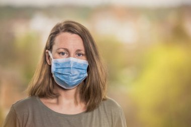 Coronavirus, koruyucu maskeli kadın dışarıdaki kameraya bakıyor. Salgın COVID-19 konsepti. Kopyalama alanı ile seçmeli odak.