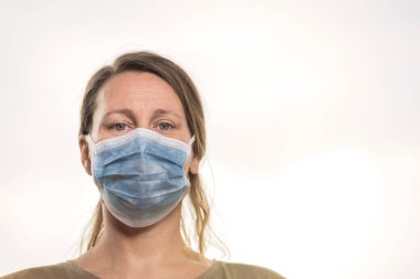 Coronavirus, koruyucu maskeli kadın, kameraya bakıyor. Hafif arkaplan. Salgın COVID-19 konsepti. Kopyalama alanı ile seçmeli odak.