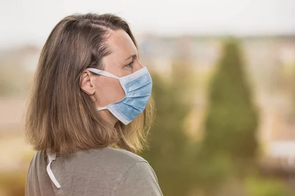 Coronavirus açık hava portresi, koruyucu maskeli kadın yana bakıyor. COVID-19 kavramı. Kopyalama alanı ile seçmeli odak.
