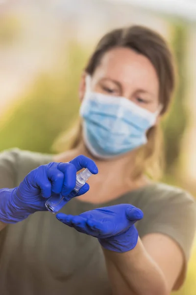 Dur Coronavirus, koruyucu tıbbi maskeli ve ameliyat eldivenli sarışın kadın antiseptik jel kullanıyor. Salgın önleme COVID-19 konsepti.