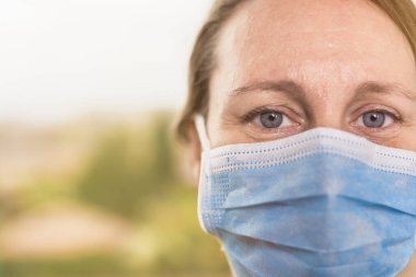 Coronavirus salgını konsepti, kameraya bakan koruyucu maskeli kadın gözlerinin portresi. COVID-19. Kopyalama alanı ile seçmeli odak.