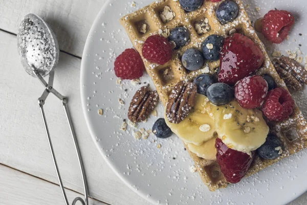 Muz dilimleri, yulaf, ceviz ve böğürtlenli waffle beyaz kırsal ahşap bir masanın üzerinde servis edilir. Üst görünüm.