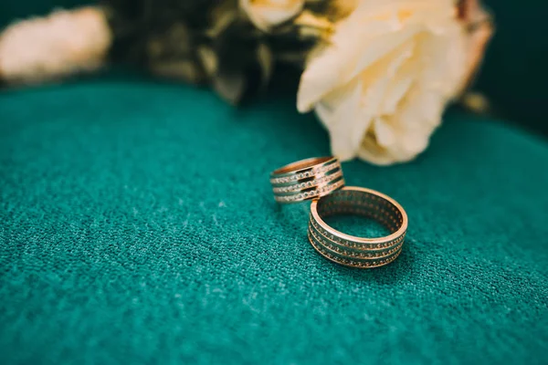 Beautiful wedding rings lie on a wooden surface against the background of a bouquet of flowers — Stock Photo, Image