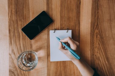 İş ve ofis kavramı. Not Defteri'nde yazma kız. Telefon ve cam. Ahşap arka plan üzerinde.