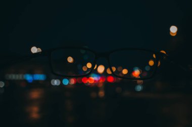 Gece cityscape gökdelenler ve bir çift gözlük görüldüğü gibi şehir ışıkları ile. Bulanık resim.