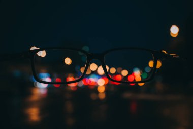 Gece cityscape gökdelenler ve bir çift gözlük görüldüğü gibi şehir ışıkları ile. Bulanık resim.