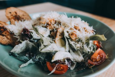 Tavuklu Sezar salatası ve ahşap masada yeşiller.