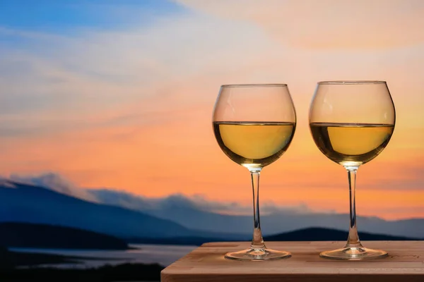 Renkli günbatımında sahilde romantik bir kadeh şarap. Gün batımına karşı beyaz şarap kadehleri, gökyüzünde bulutlu beyaz şarap.