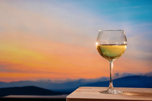 Renkli günbatımında sahilde romantik bir kadeh şarap. Gün batımına karşı beyaz şarap kadehleri, gökyüzünde bulutlu beyaz şarap.