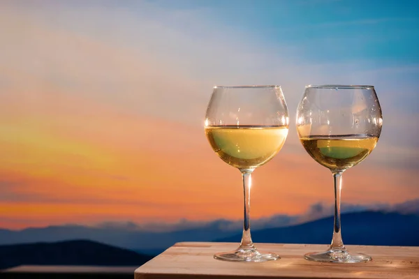 Renkli günbatımında sahilde romantik bir kadeh şarap. Gün batımına karşı beyaz şarap kadehleri, gökyüzünde bulutlu beyaz şarap.