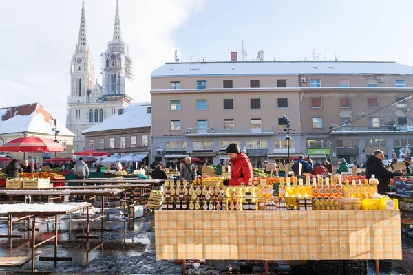 Zagreb, Croácia: 7 de janeiro de 2016: Stand with honey glasses at Dolac market during wintertime with snow with cathedral in the back — Fotografia de Stock