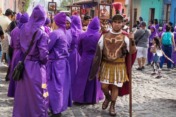 Hombre con traje de soldado romano caminando a lo largo de hombres vestidos de púrpura en la procesión de San Bartolomé de Becerra en 1a Avenida, Antigua Guatemala —  Fotos de Stock